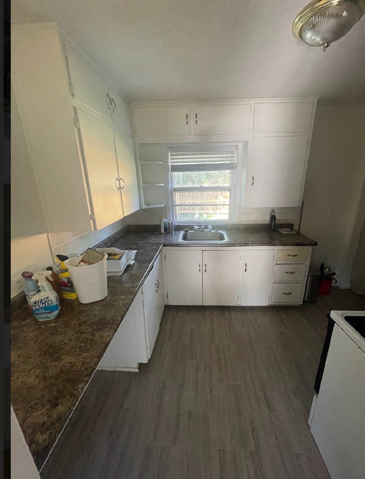 White kitchen with cabinets, window over sink, brown countertops, and gray flooring.