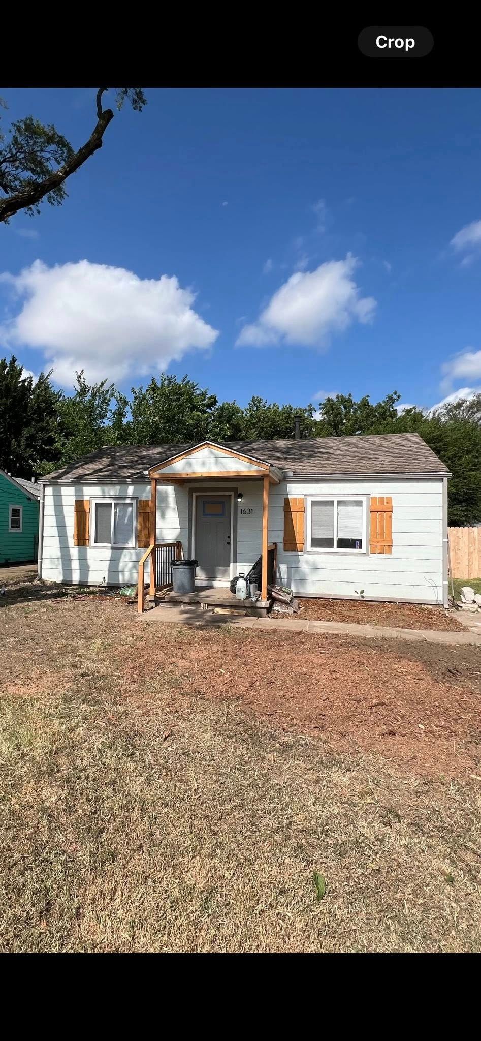 White house with brown shutters and a porch, set against a blue sky with trees.