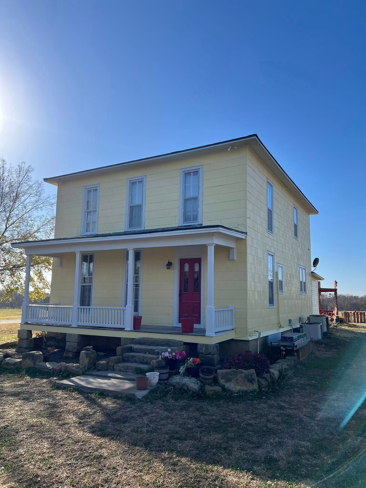 Yellow two-story house with a red door, white porch, and several windows on a sunny day.