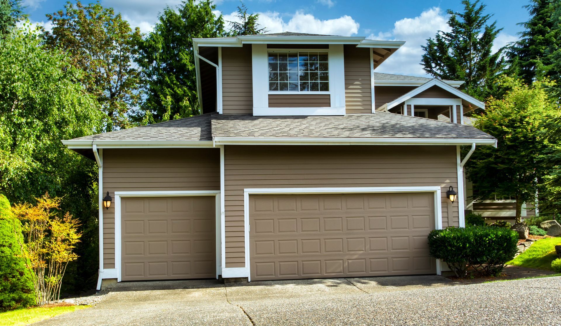 Two-story tan house with a two-car garage, white trim, and trees.