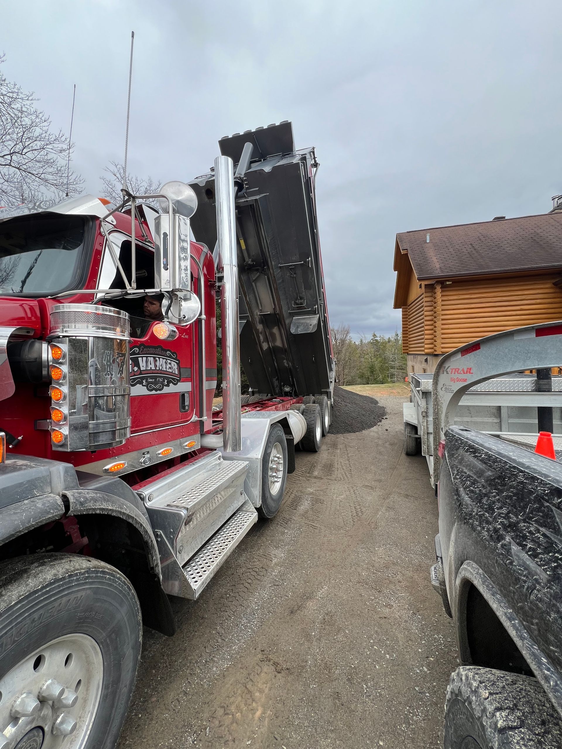 Un camion-benne rouge roule sur un chemin de terre à côté d'un camion noir.
