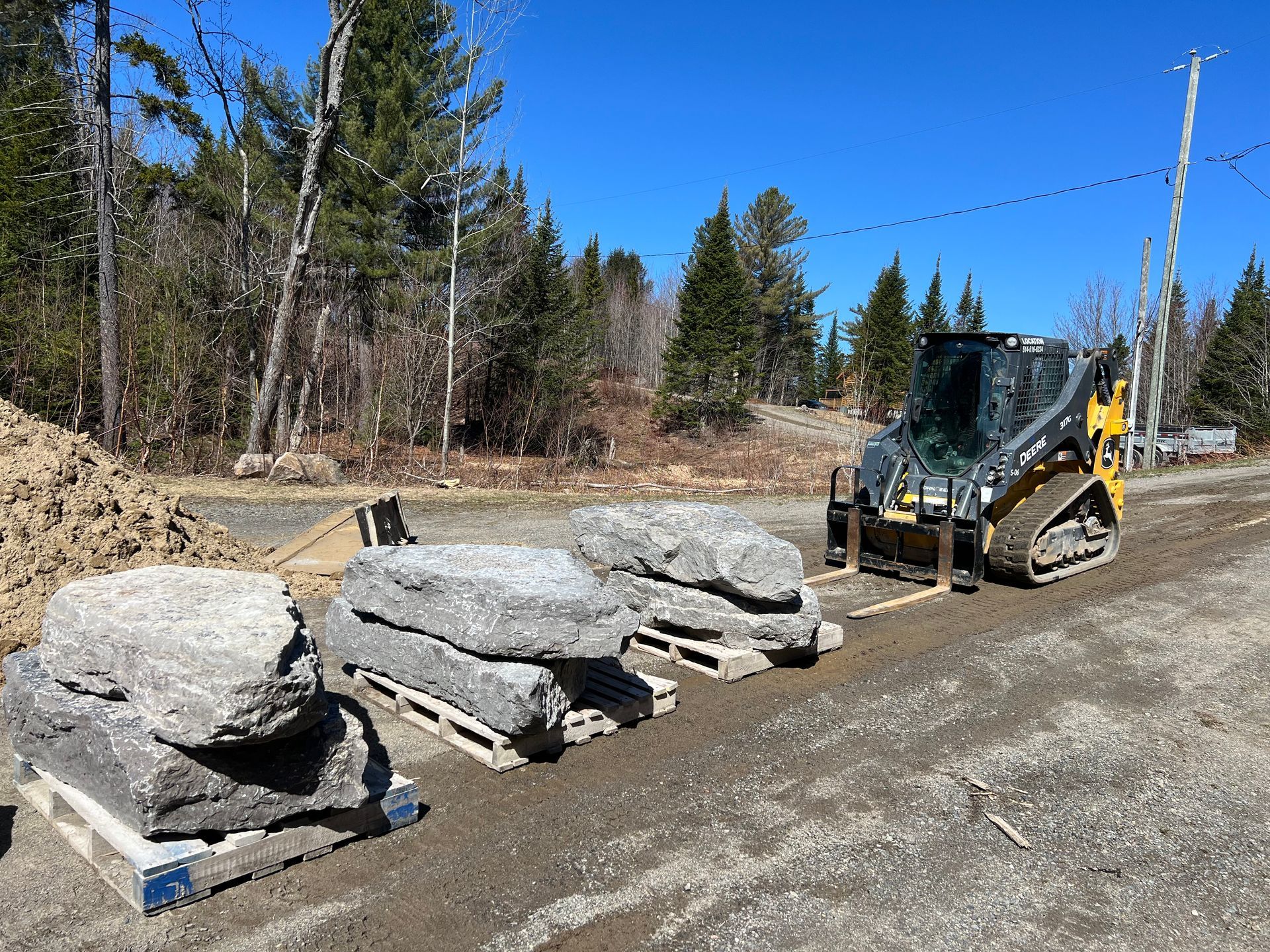 Un bulldozer déplace des rochers sur des palettes sur le bord de la route.