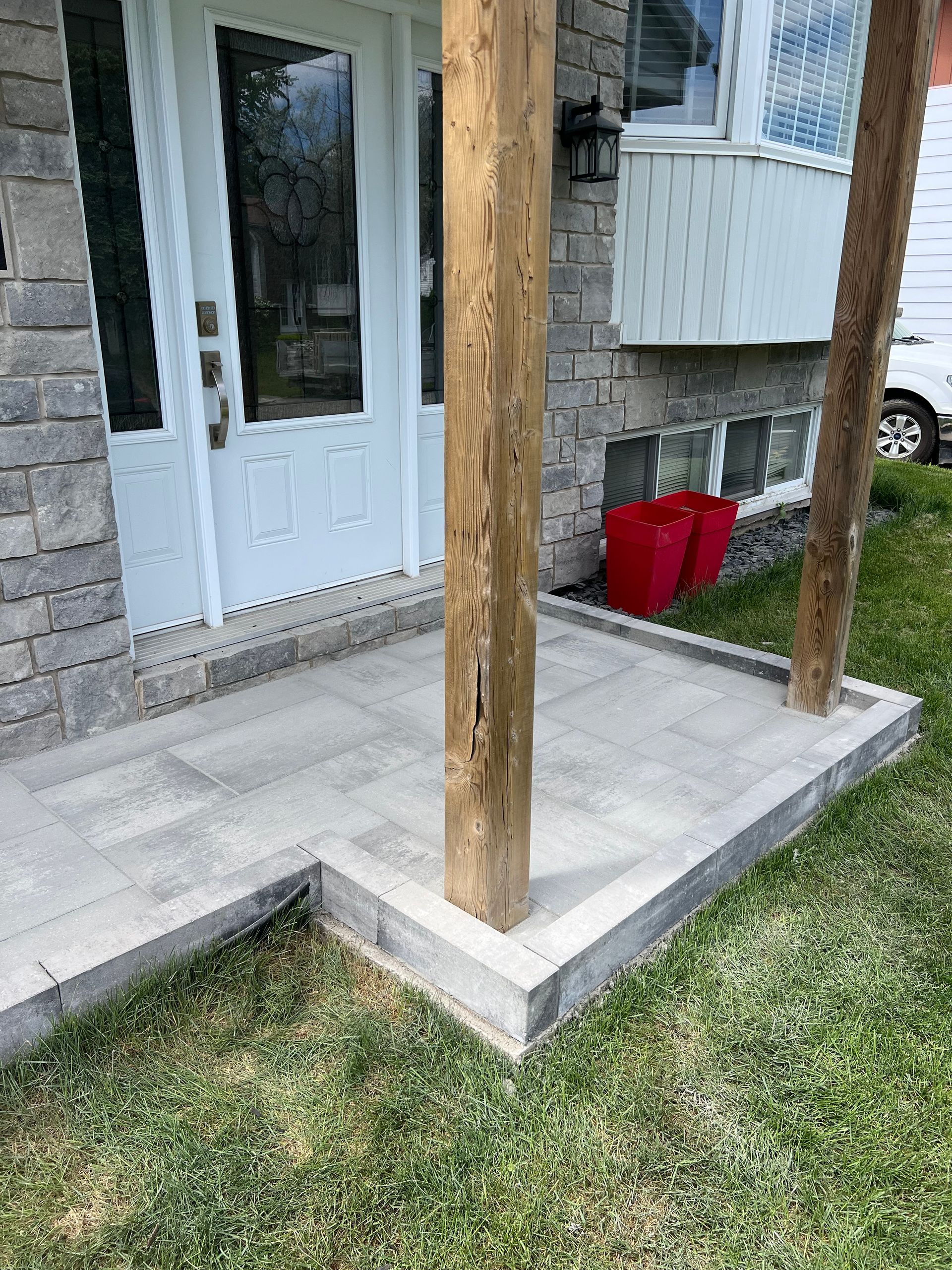 Un porche avec un poteau en bois devant une maison en brique.