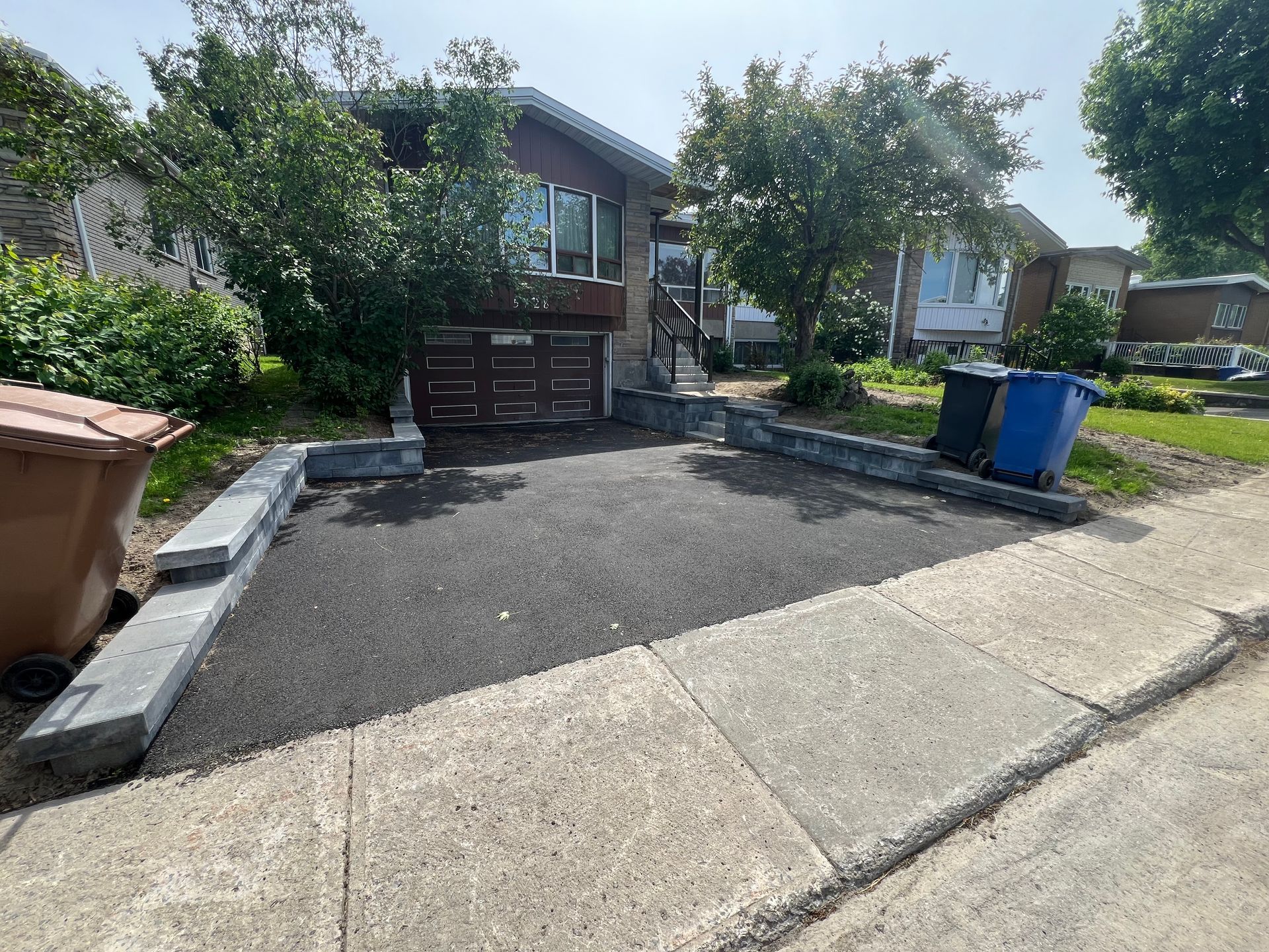 Une maison avec une allée et des poubelles devant.