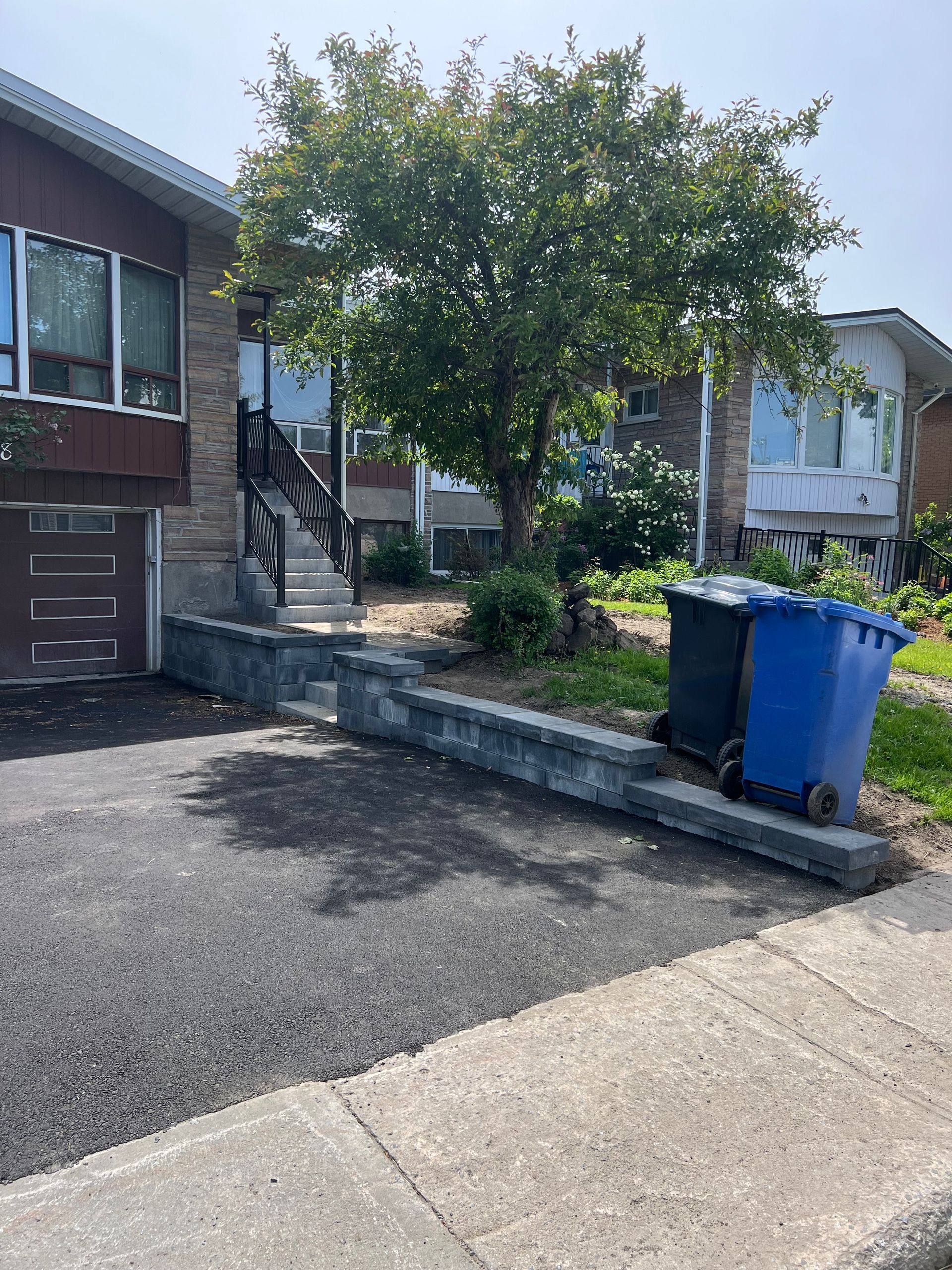 Une poubelle bleue se trouve sur le trottoir devant une maison.