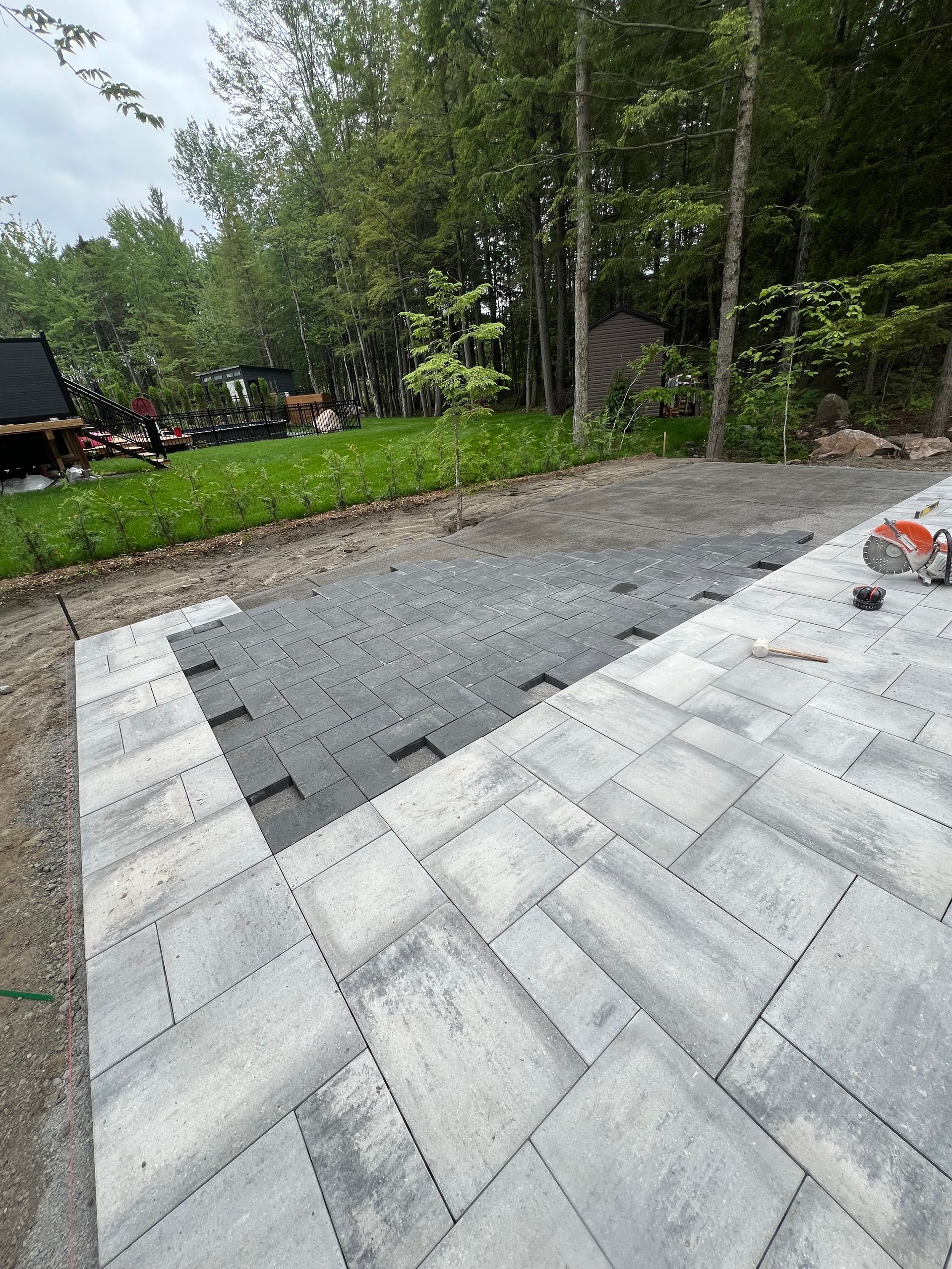 Un patio est en cours de construction dans une cour arrière avec des arbres en arrière-plan.