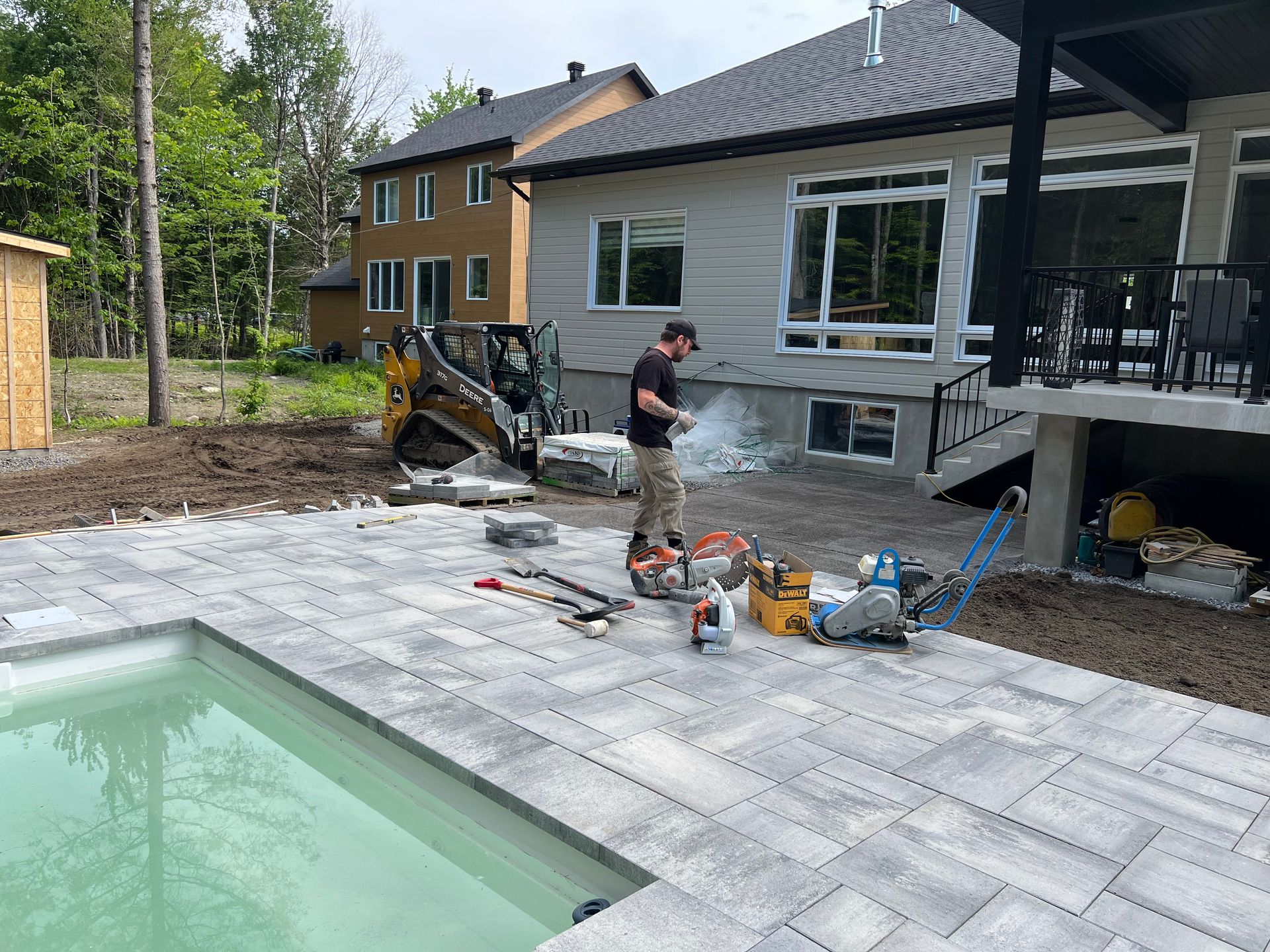 Un homme travaille sur une terrasse à côté d'une piscine devant une maison.