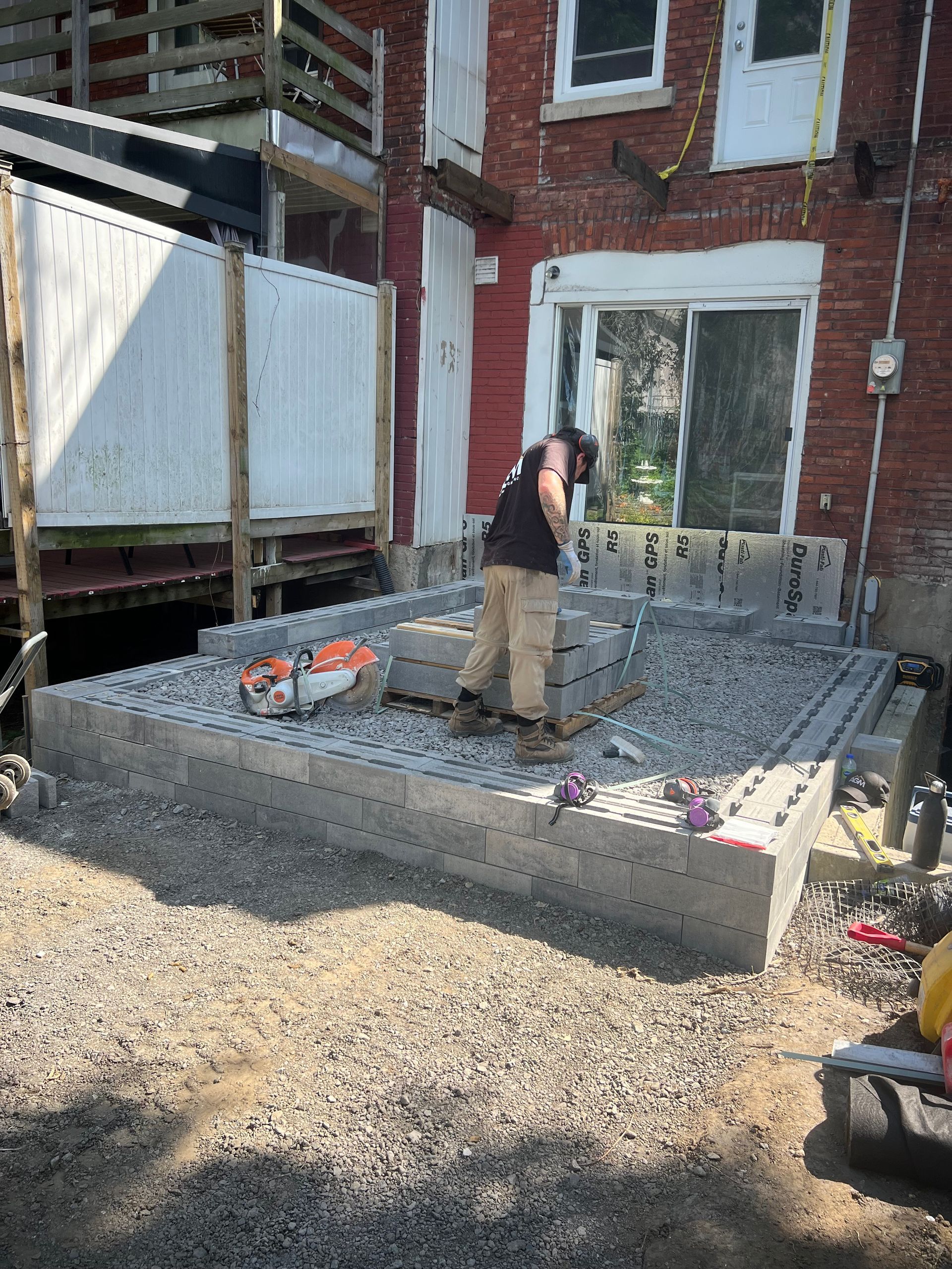 Un homme se tient debout sur un tas de gravier devant un bâtiment en briques.