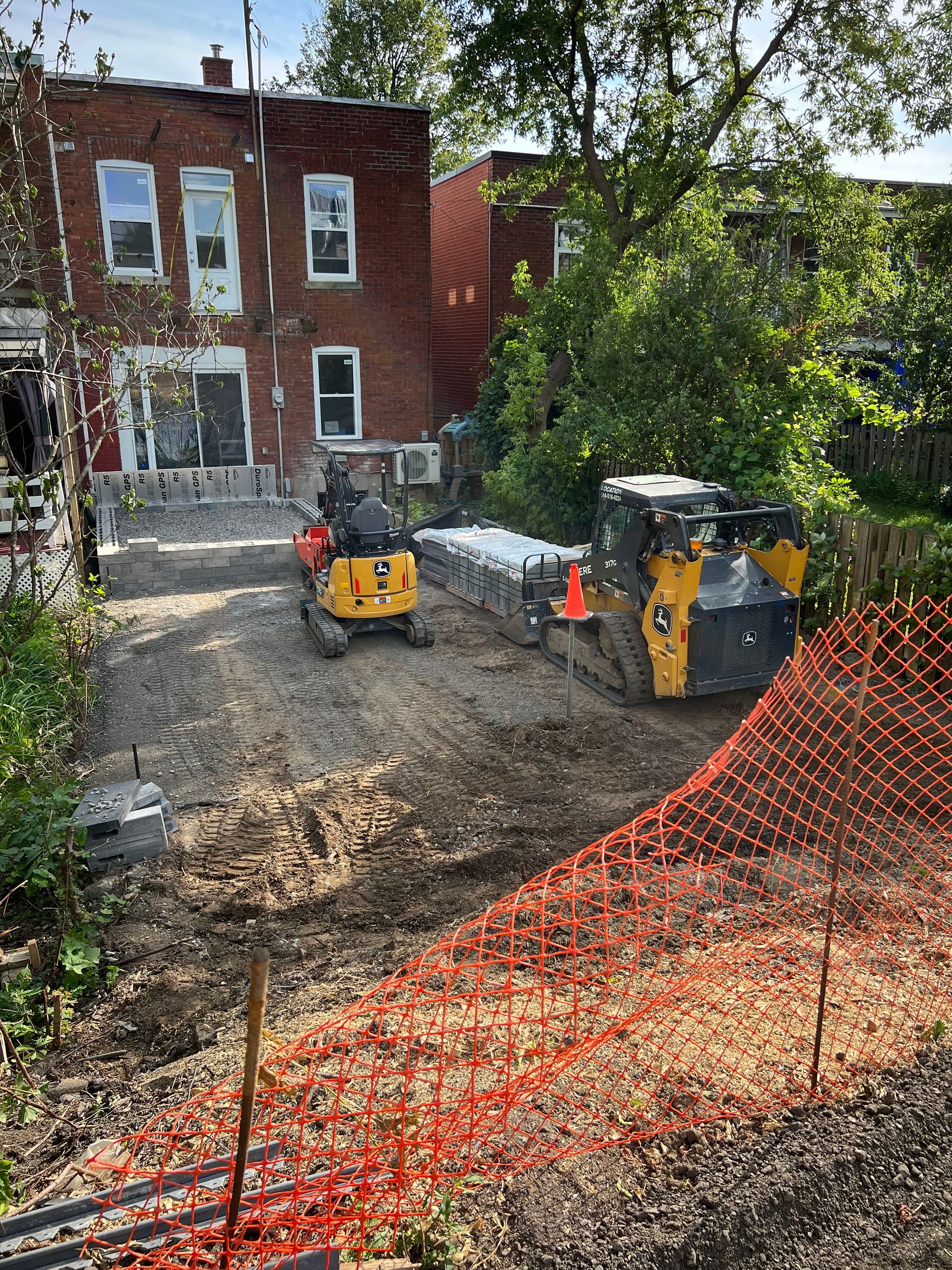 Un couple de tracteurs roule sur un chemin de terre devant un bâtiment en briques.
