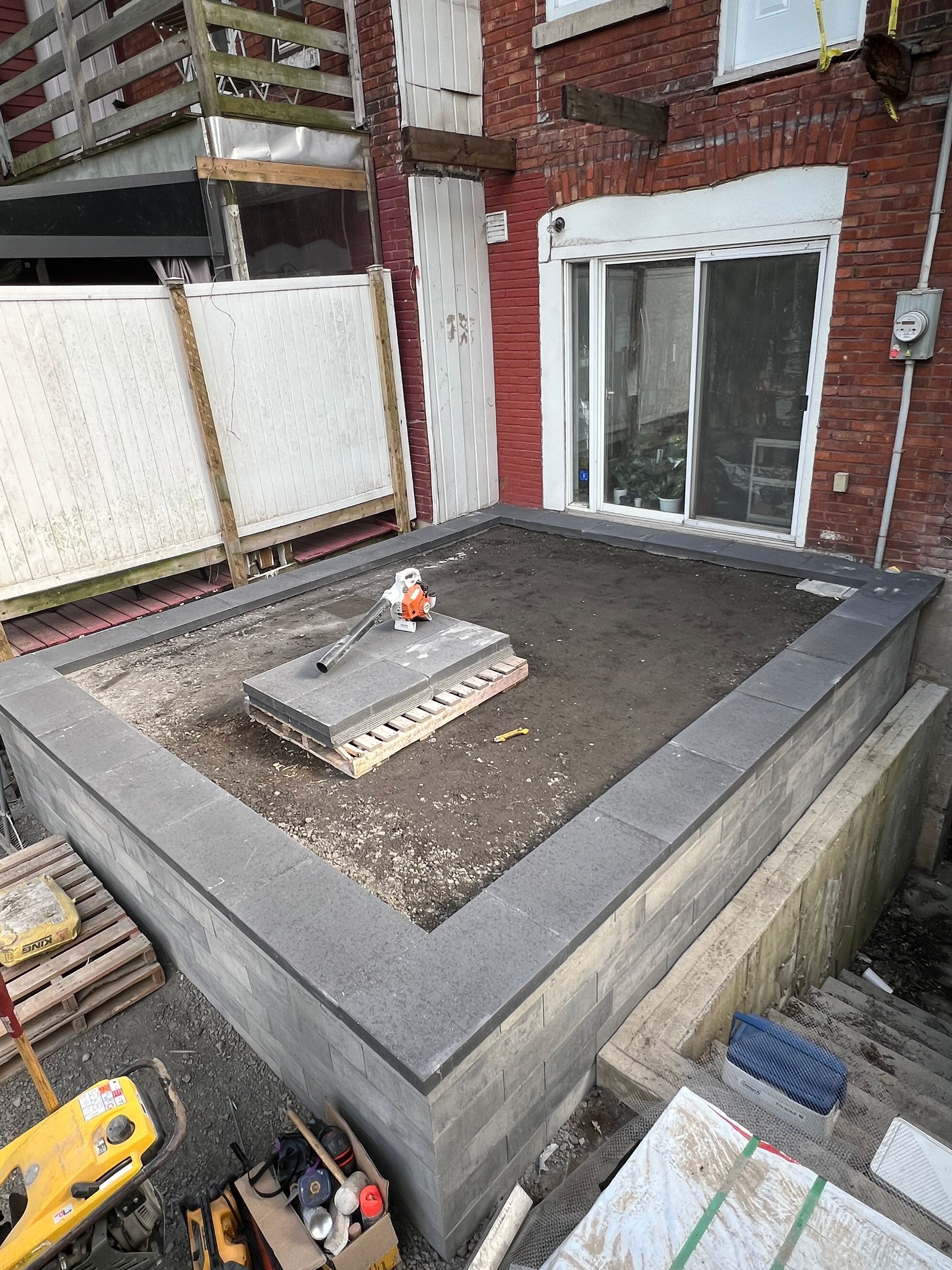 Une grande plateforme en béton est en cours de construction devant un bâtiment en briques.