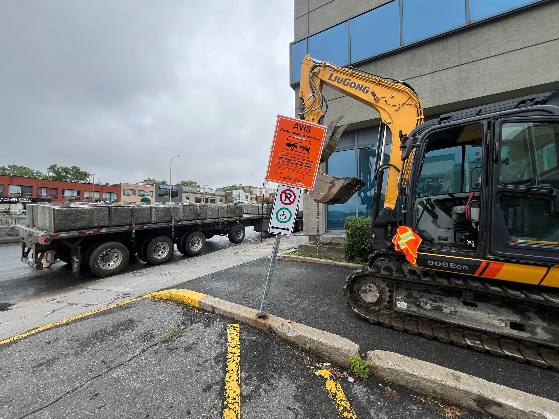 Une excavatrice creuse un trou dans un parking à côté d'un camion.