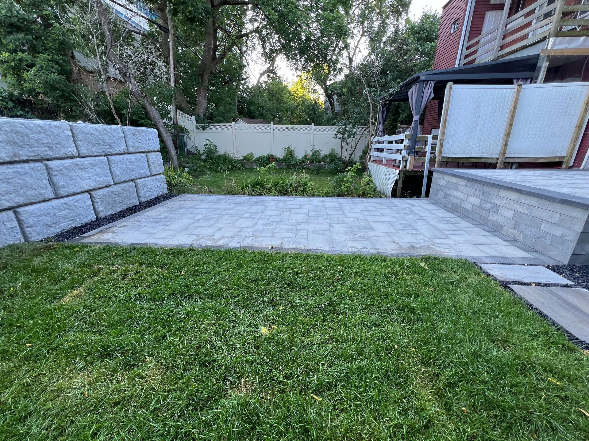 Une cour arrière avec un mur de briques, un patio et une pelouse verte luxuriante.