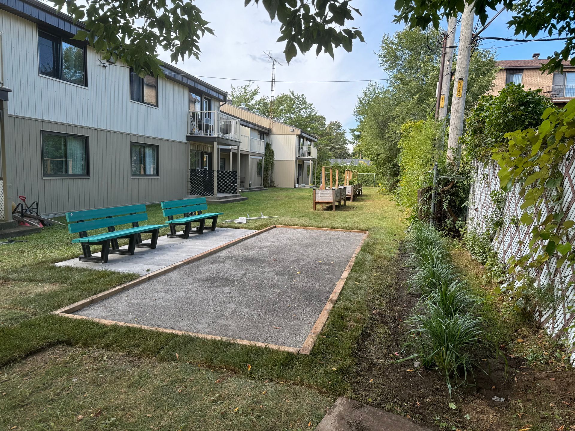 Un terrain de pétanque devant un bâtiment avec des bancs bleus.