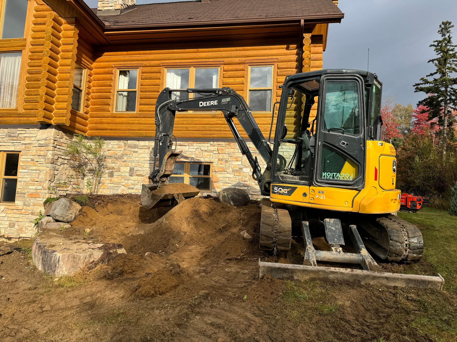 Une excavatrice jaune creuse un trou devant une cabane en rondins.