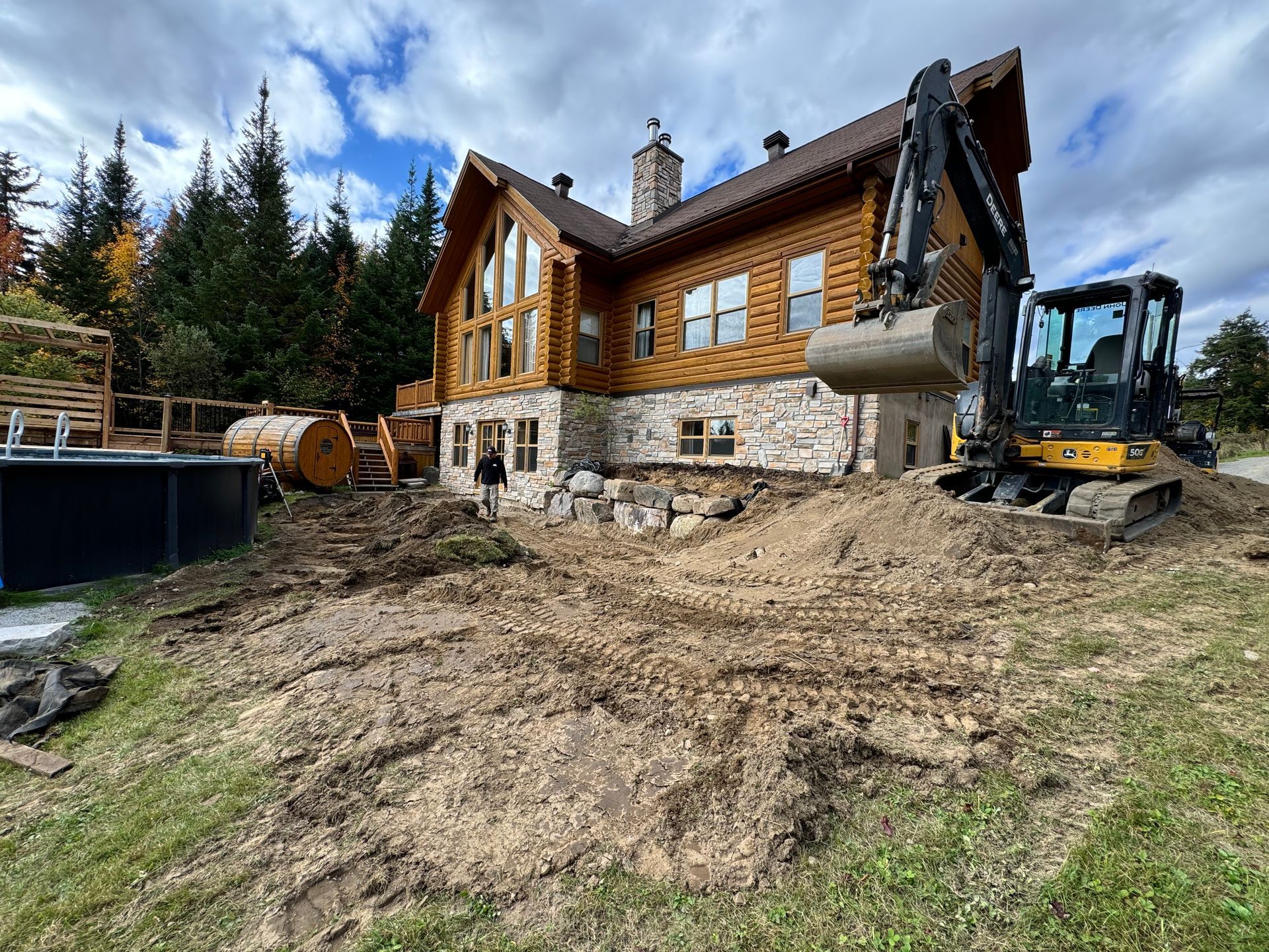 Une grande cabane en rondins est en cours de construction avec une grande excavatrice devant elle.