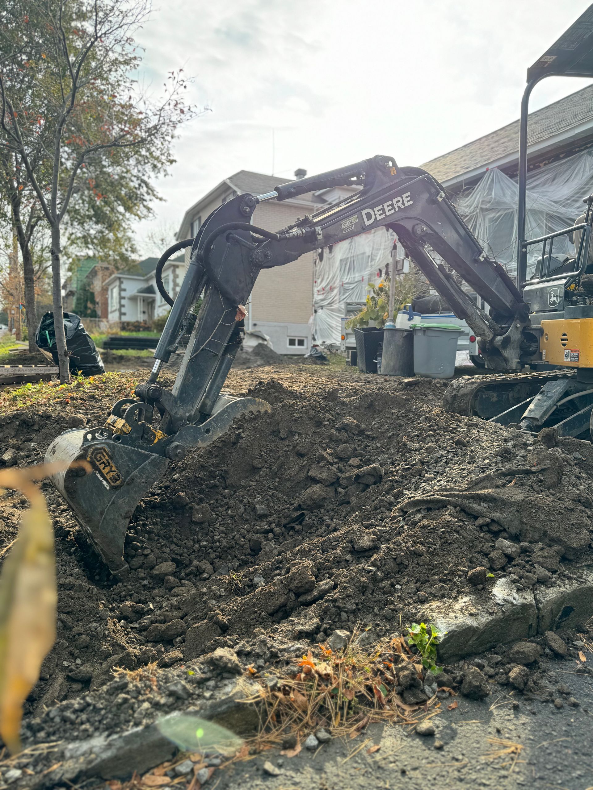 Une grande excavatrice creuse un trou dans le sol devant une maison.