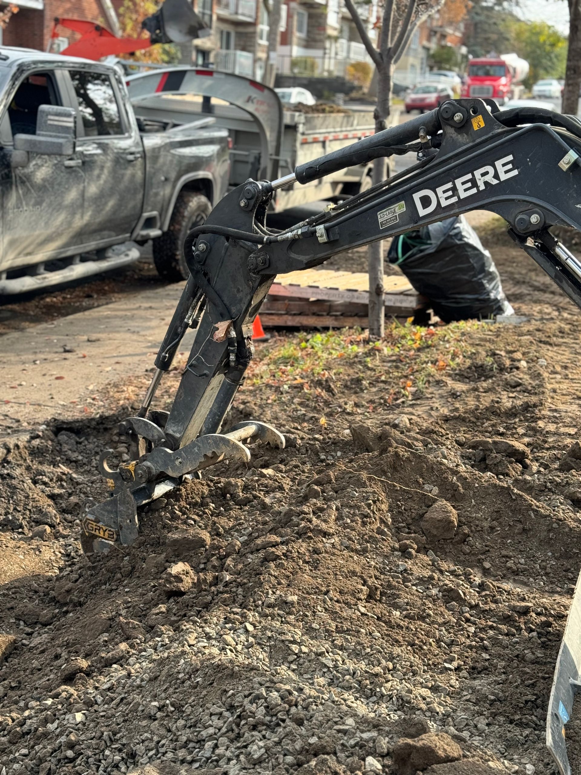 Une excavatrice Deere creuse un trou dans la terre à côté d'un camion.