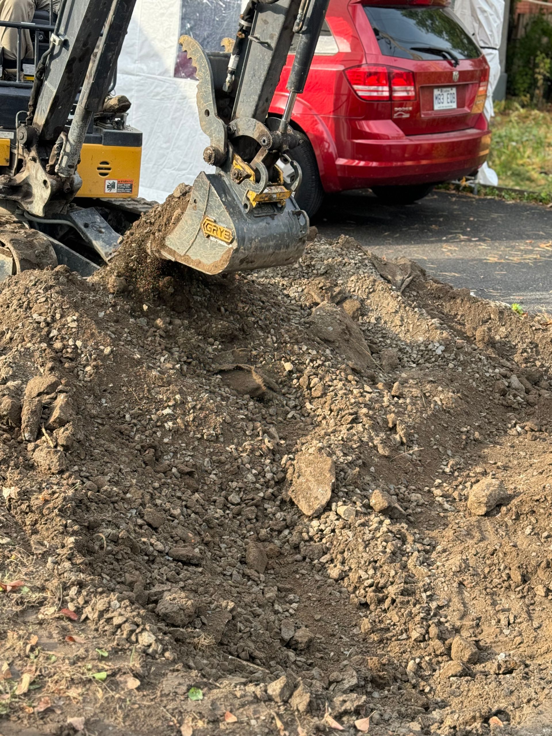 Une voiture rouge est garée devant un tas de terre.