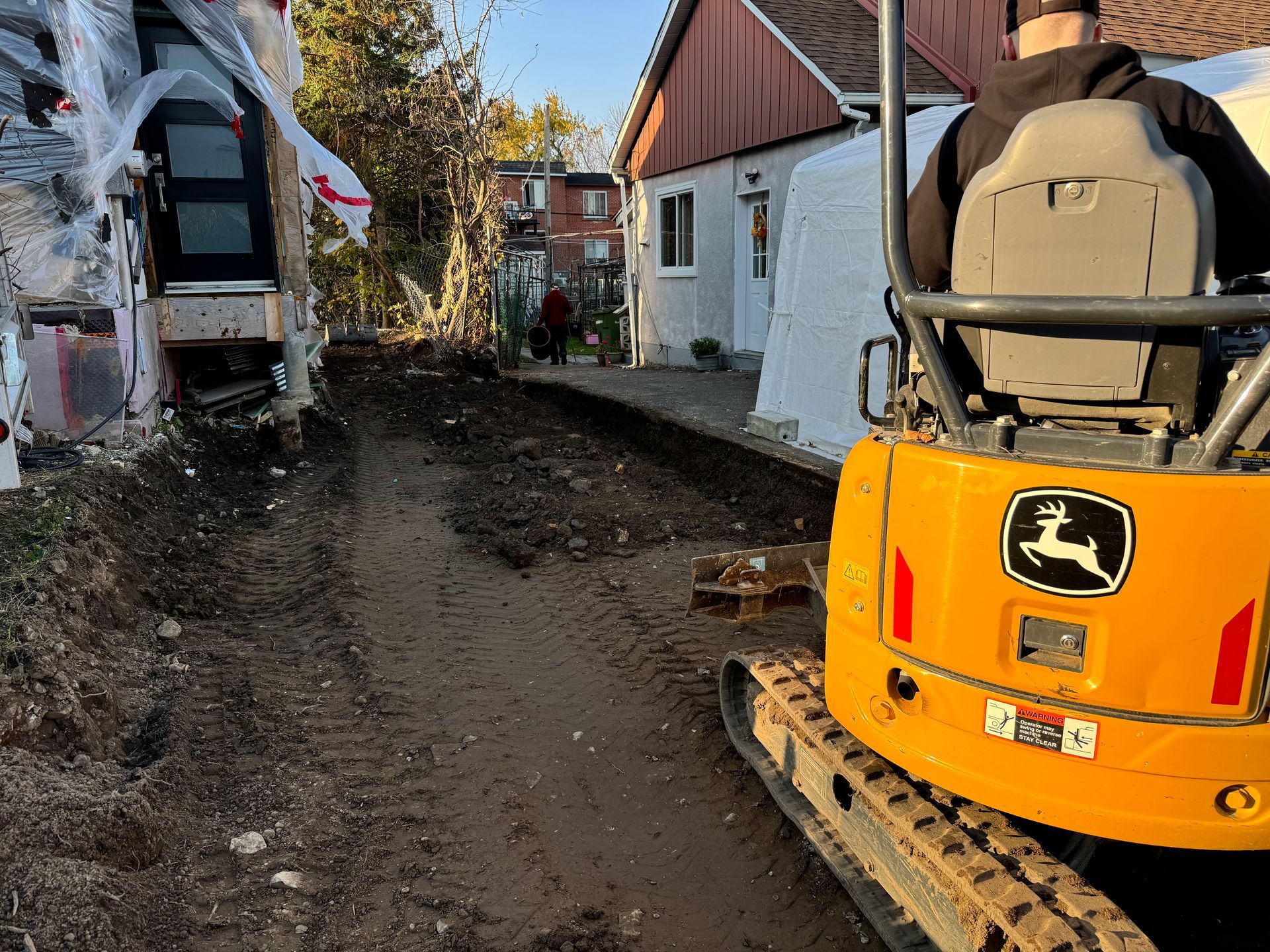 Un homme conduit une excavatrice John Deere jaune sur un chemin de terre.