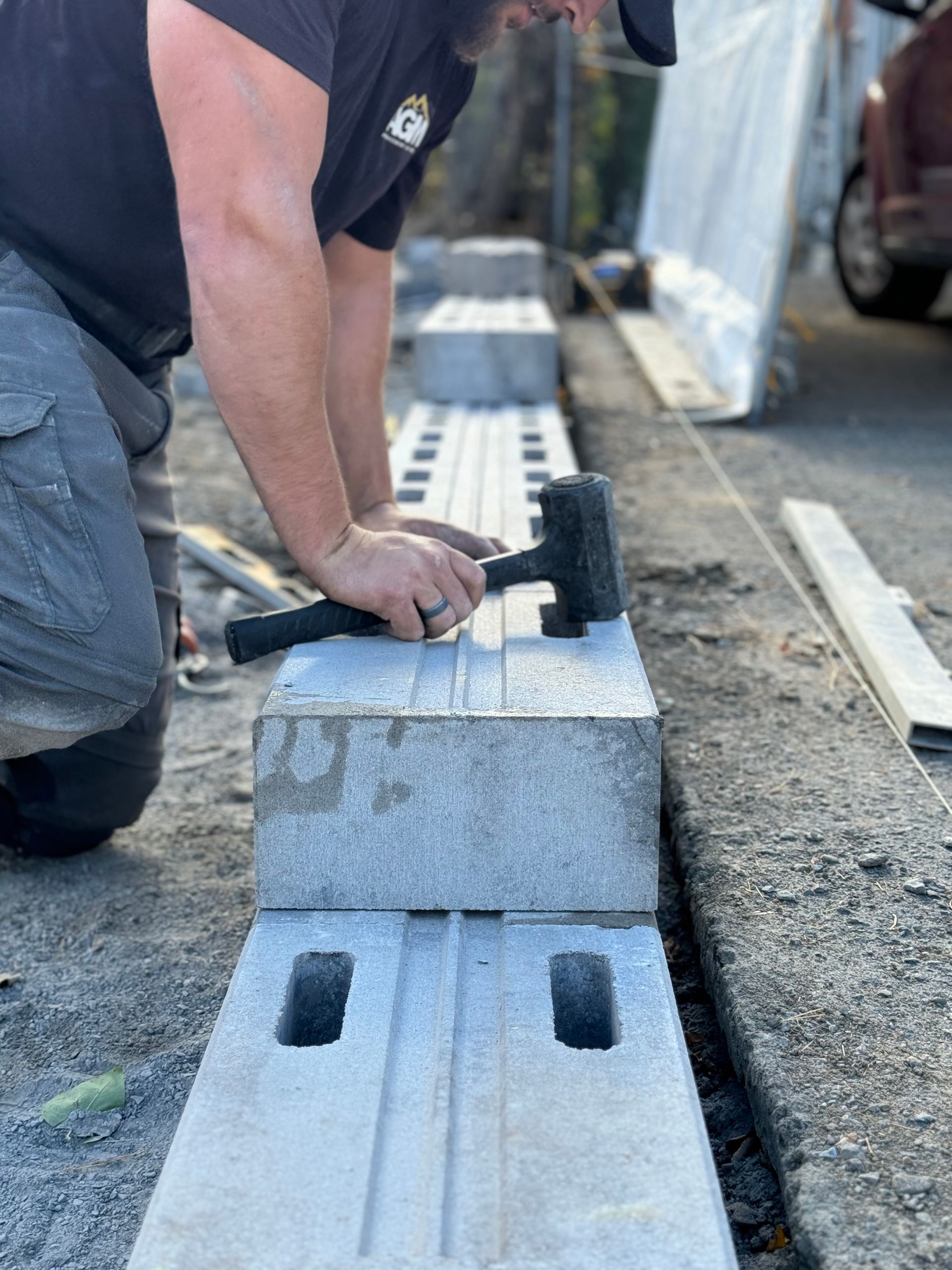 Un homme est à genoux et utilise un marteau pour marteler un bloc de béton.