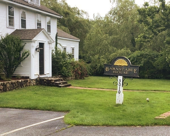 A barnstable house sign is in front of a white house