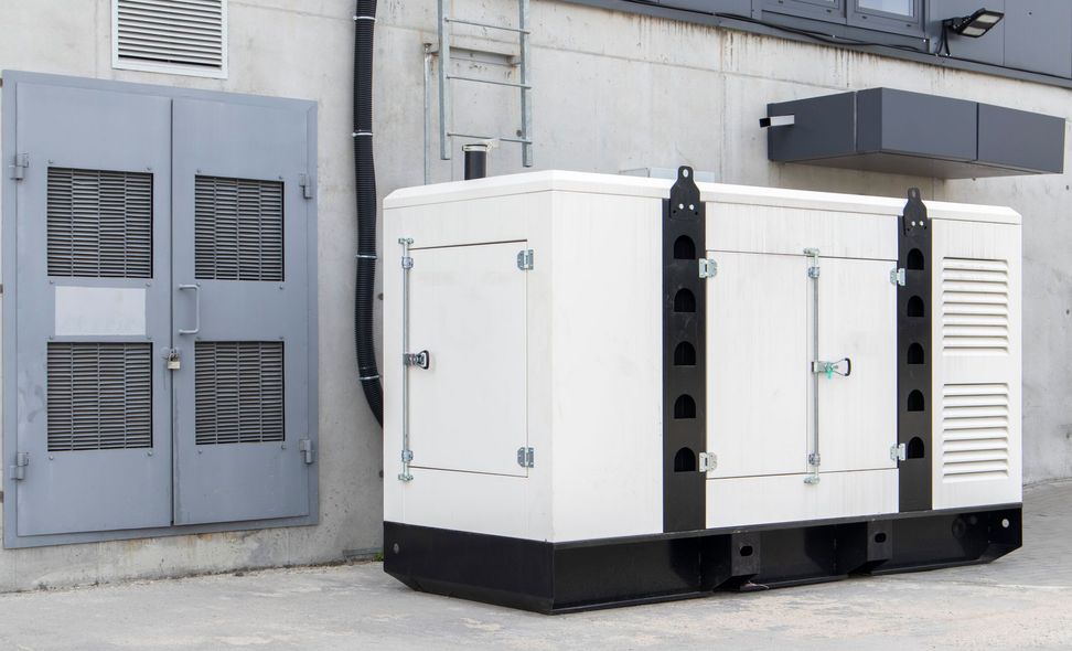 White generator unit against a building wall. A grey door is to the left.
