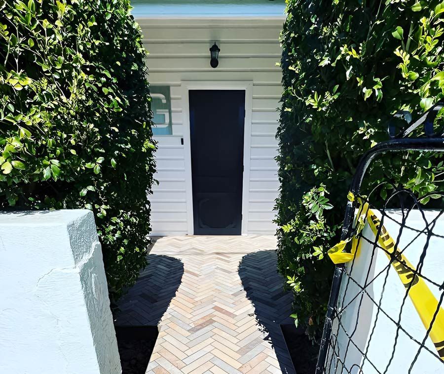 A Walkway Leading to a House With a Black Door Surrounded by Bushes — S & S Tiling and Rendering in Bourke, NSW