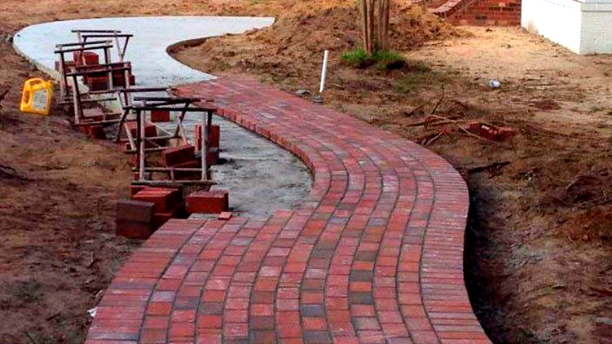 Red brick path under construction, curving through a dirt yard in Fayetteville, NC.