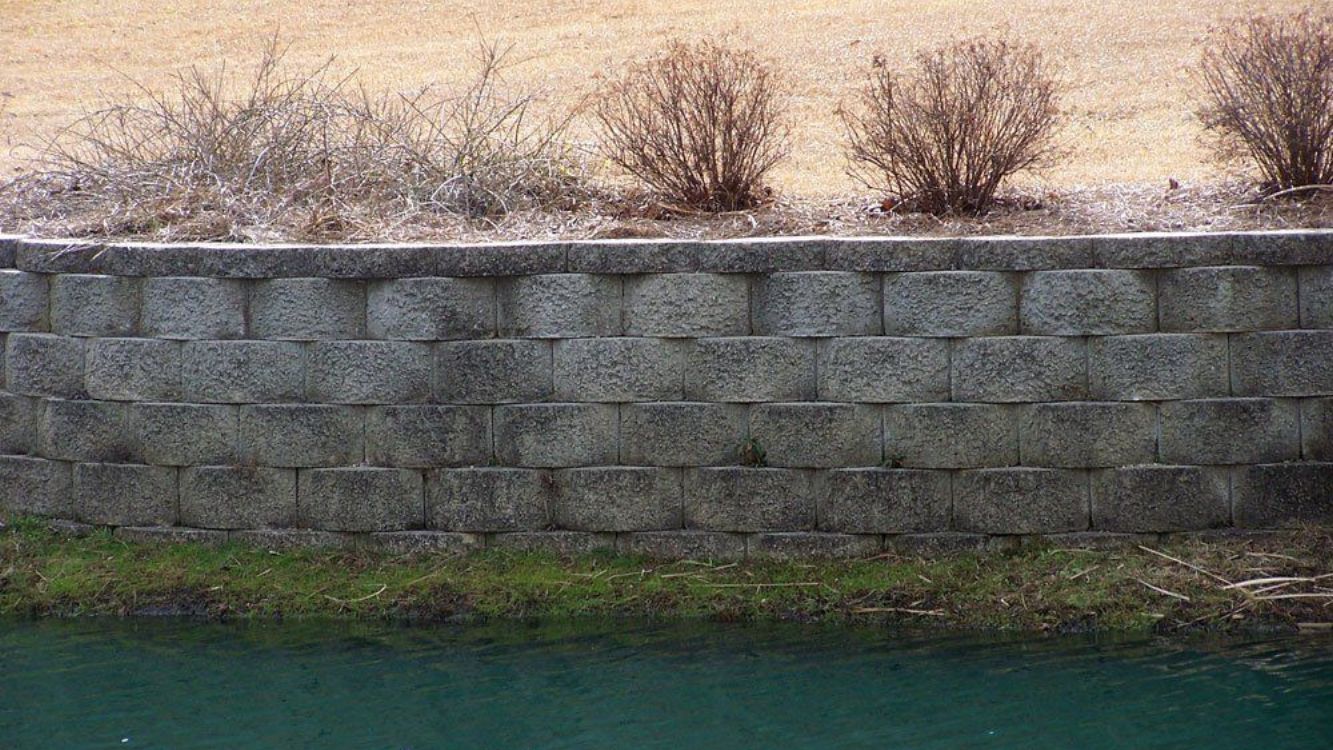 Stone retaining wall with shrubs on top, near water in Fayetteville, NC.