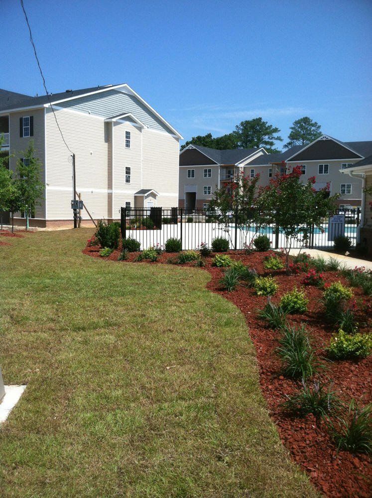 A lush green yard with a fence and a building in the background
