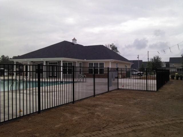 A black fence surrounds a swimming pool in front of a house