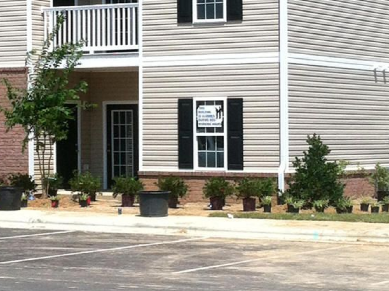 Apartment building exterior with beige siding, black shutters, brick accents, and potted plants in front in Wilmington, NC.