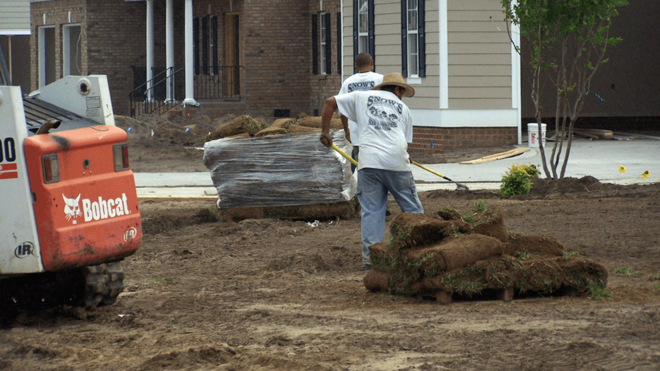 Two workers laying sod in front of a house using a Bobcat in Fayetteville, NC.