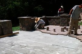 A group of men are working on a patio with bricks.