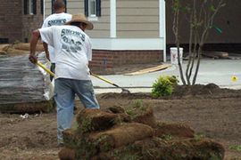 Two men are working on a lawn in front of a house.