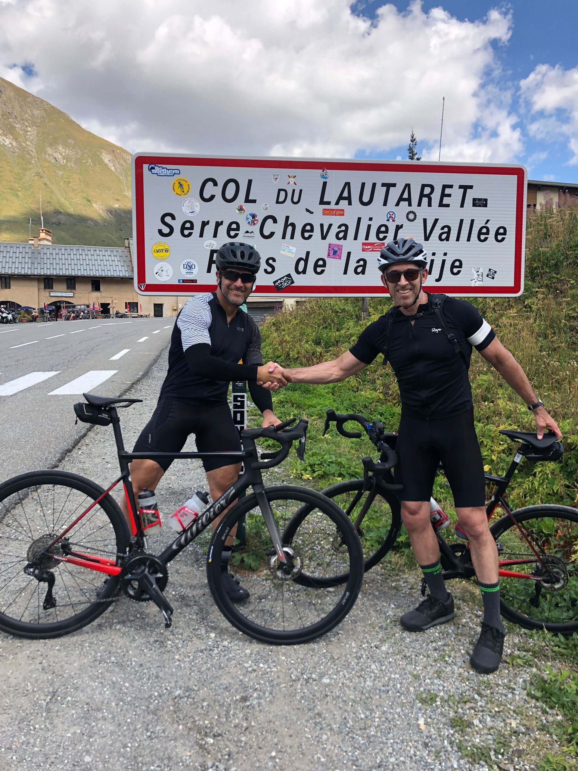Two men shaking hands in front of a sign that says col du lautaret