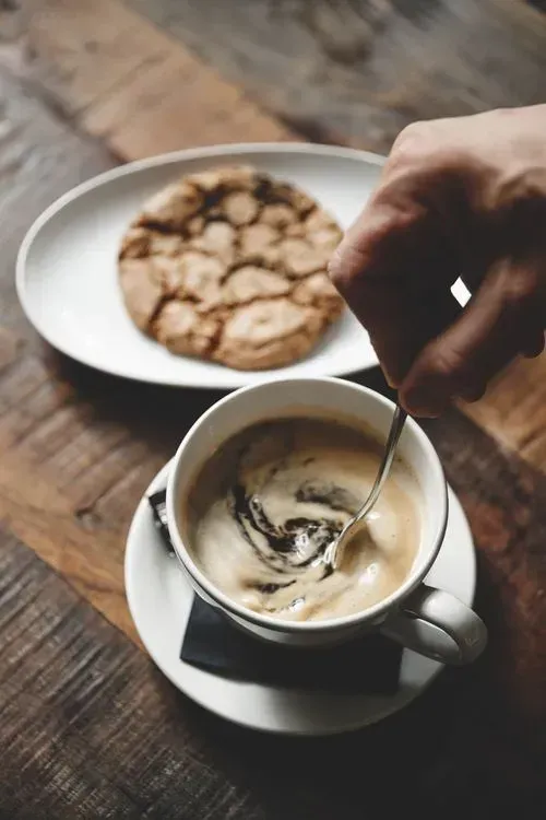 En person rører en kop kaffe med en ske.