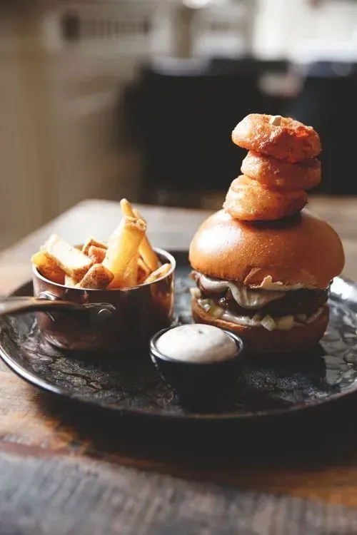 En hamburger med løgringe ovenpå og pommes frites på en tallerken.