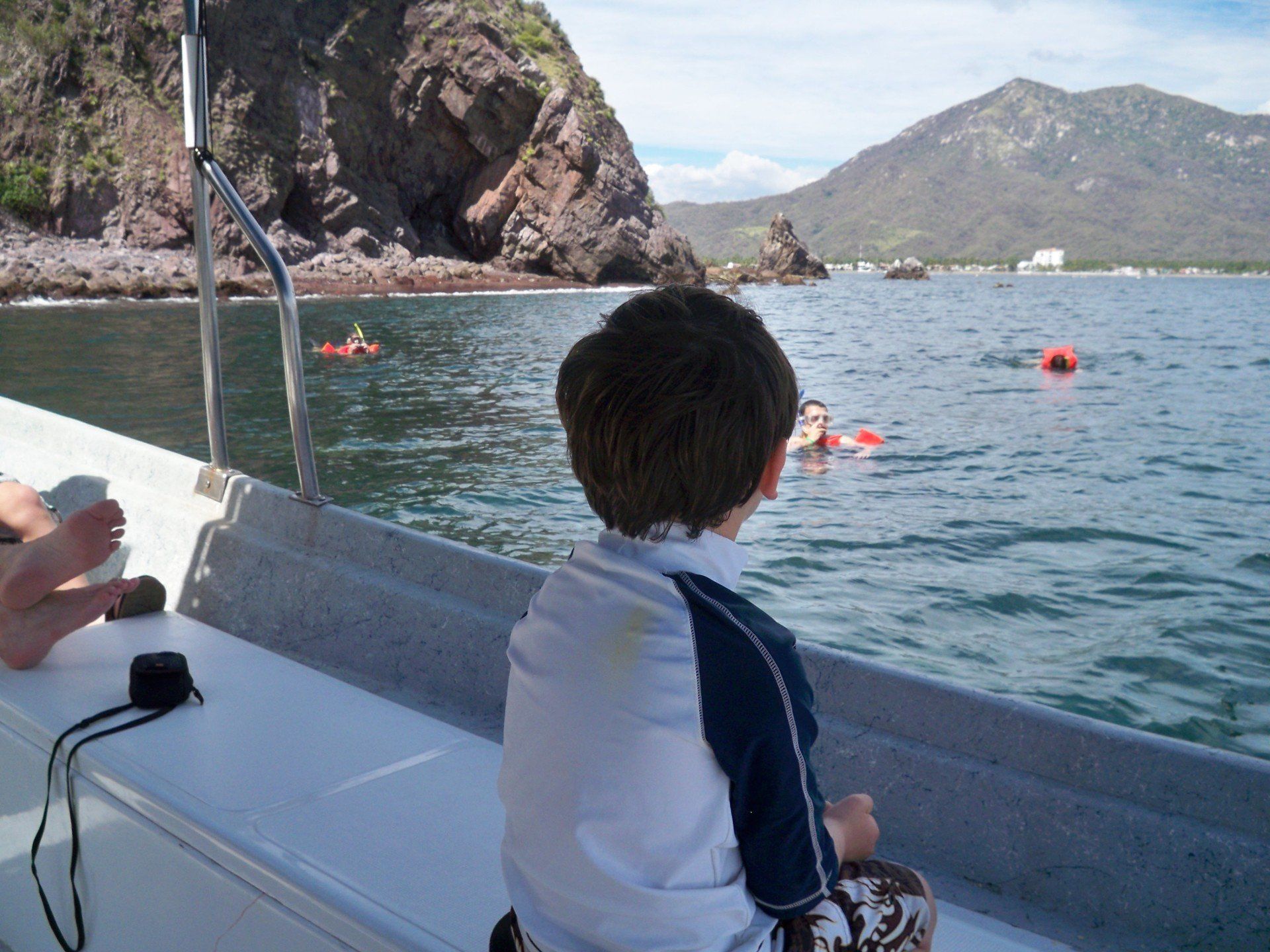 a boy sitting on a boat looking at people in the water