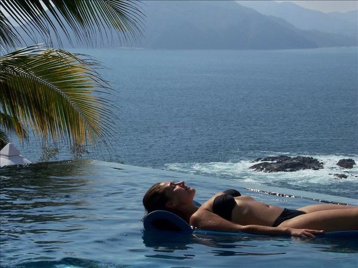a woman in a bikini is laying in an infinity pool overlooking the ocean