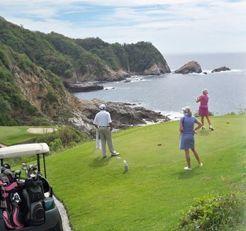 a group of people are playing golf on a golf course near the ocean .