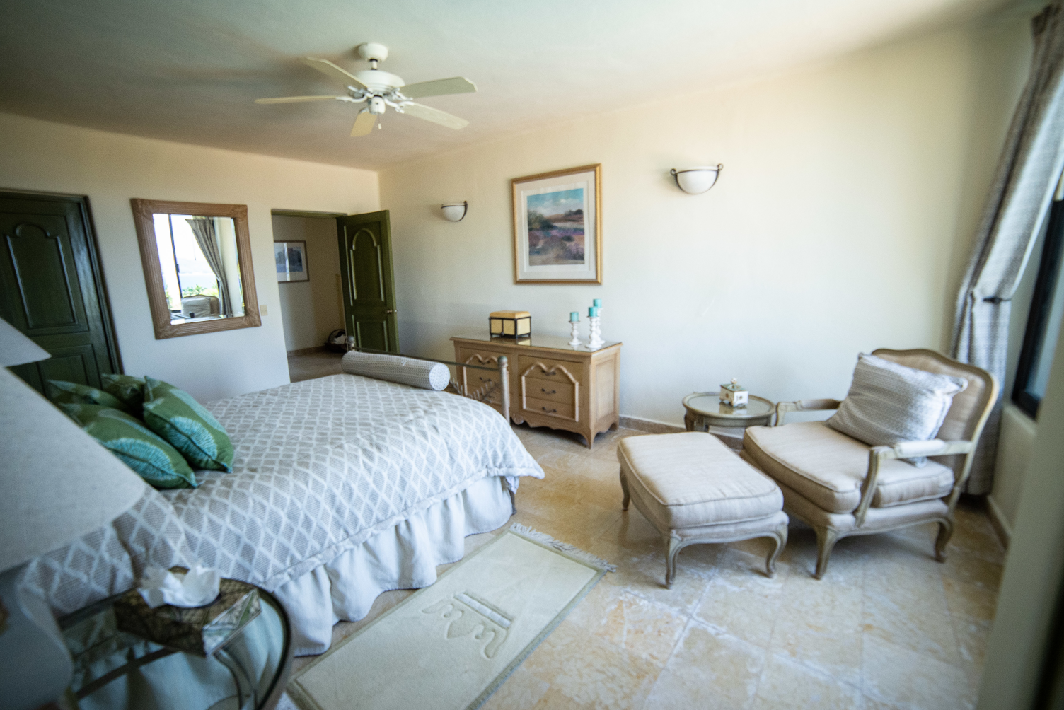 a bedroom with a bed , chairs , ottoman and a ceiling fan