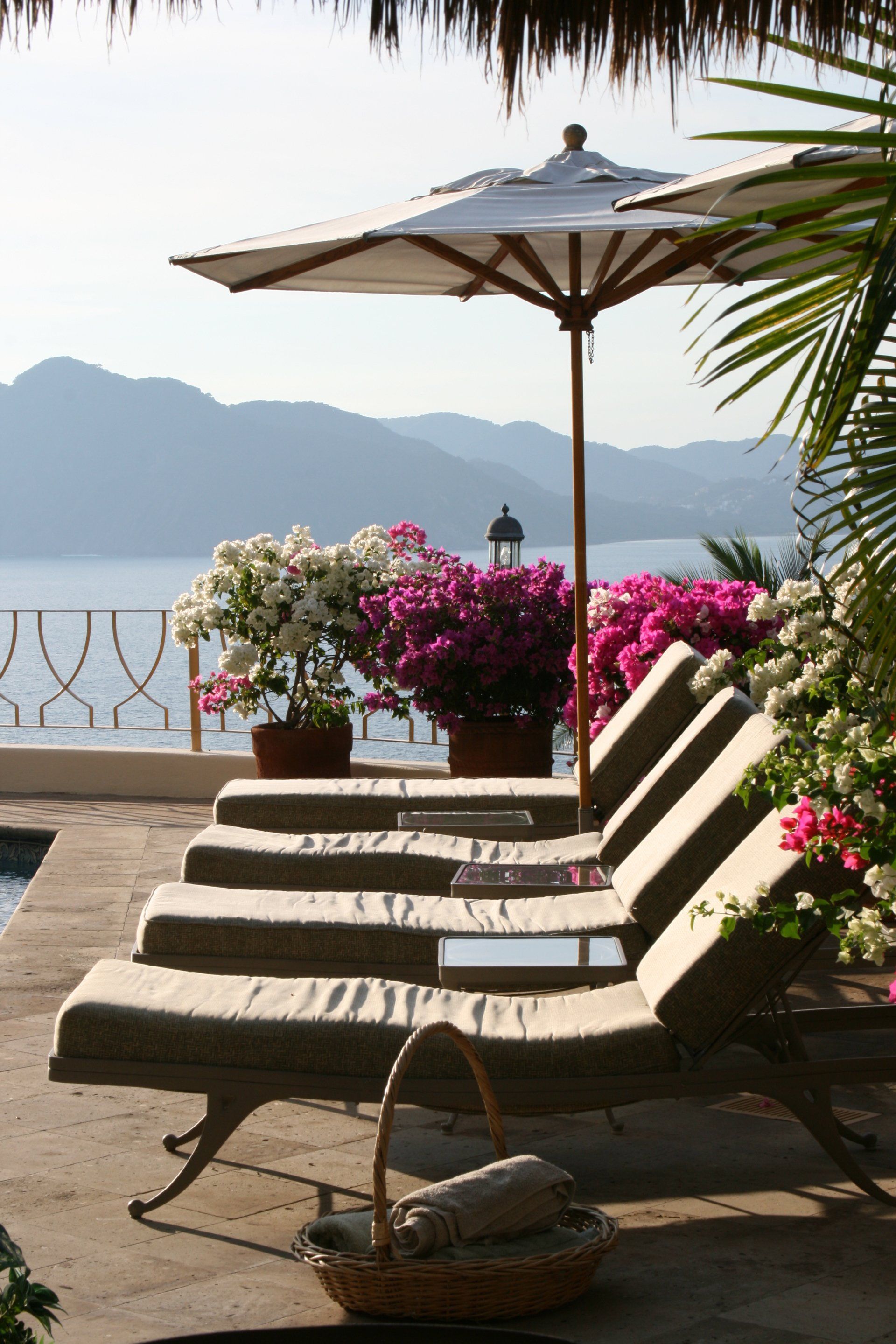a row of lounge chairs under an umbrella with mountains in the background