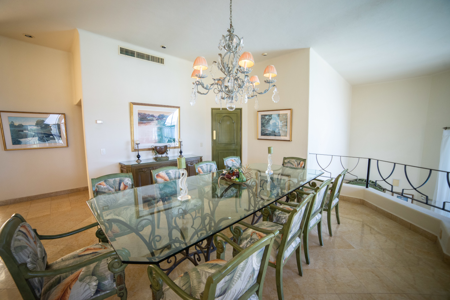 A dining room with a long glass table and chairs and a chandelier.