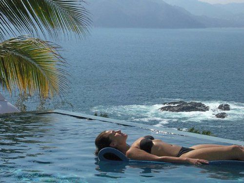 a woman in a bikini is laying in an infinity pool overlooking the ocean .