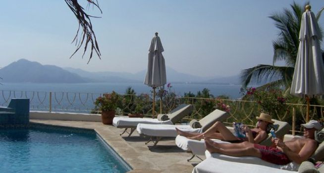 People laying on lounge chairs near a swimming pool overlooking the ocean