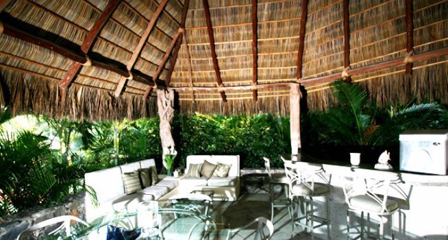 A thatched roof gazebo with a couch , table and chairs