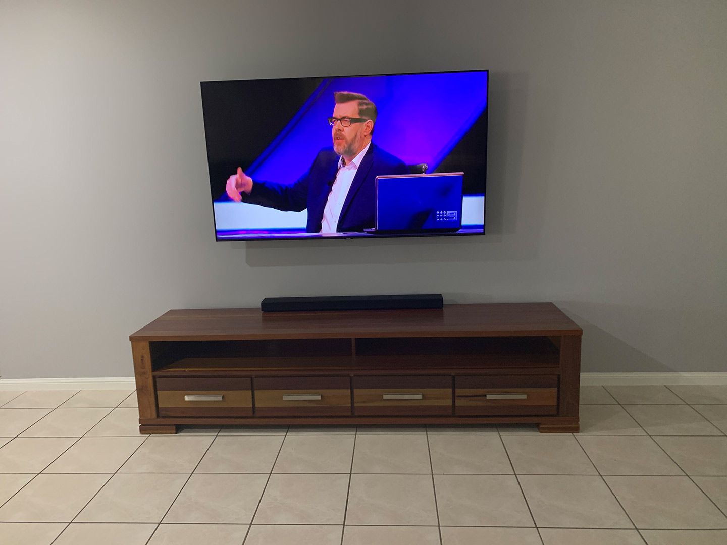 A Flat Screen Tv Is Mounted on A Wall Above a Wooden Entertainment Center — T.N. Locke Communications In Kirwan, QLD