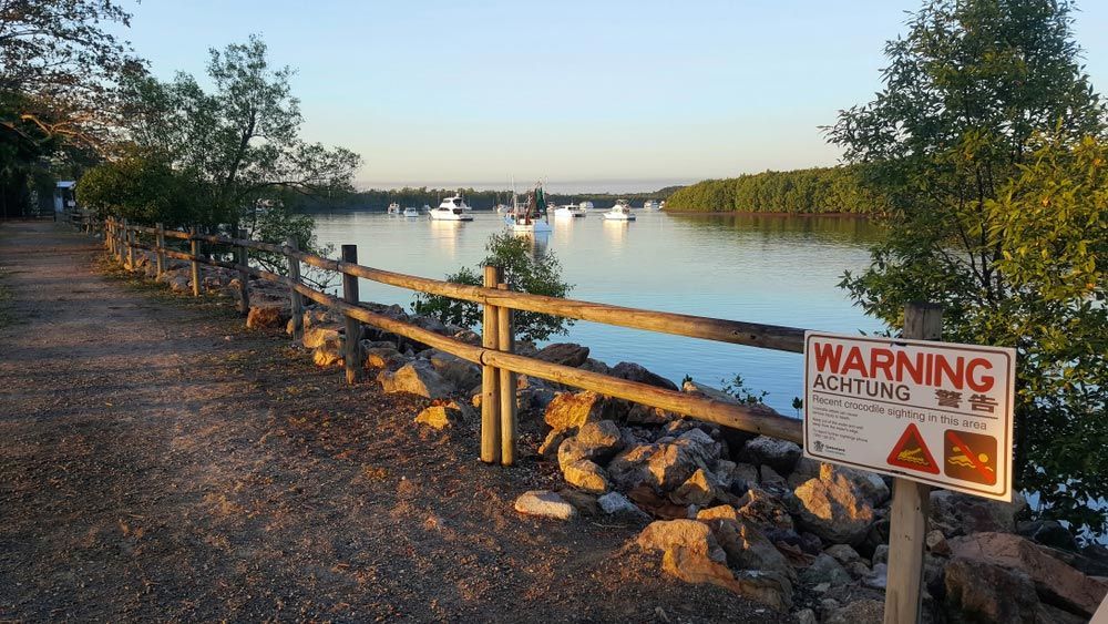 A Warning Sign is Posted on a Wooden Fence Next to a Body of Water — T.N. Locke Communications In Ingham, QLD
