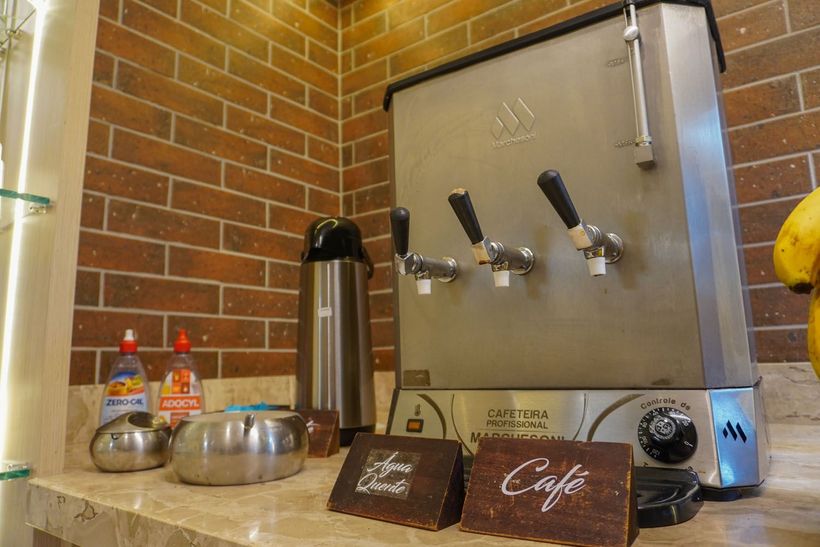 Uma máquina de café está sobre um balcão próximo a uma parede de tijolos.